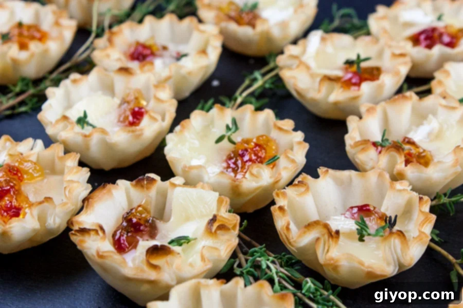 Close-up view of multiple Pepper Jelly Brie Bites on a black slate, showing melted cheese and jelly, with fresh thyme.