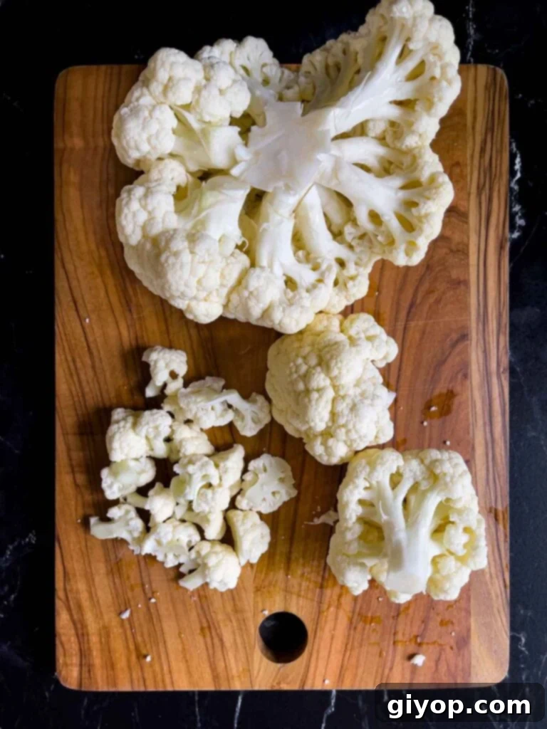Head of cauliflower being cut into small pieces on a wooden cutting board.
