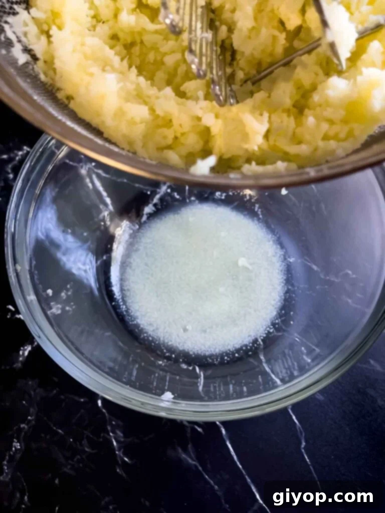 The water drained from the mashed cauliflower in the bottom of a glass bowl.
