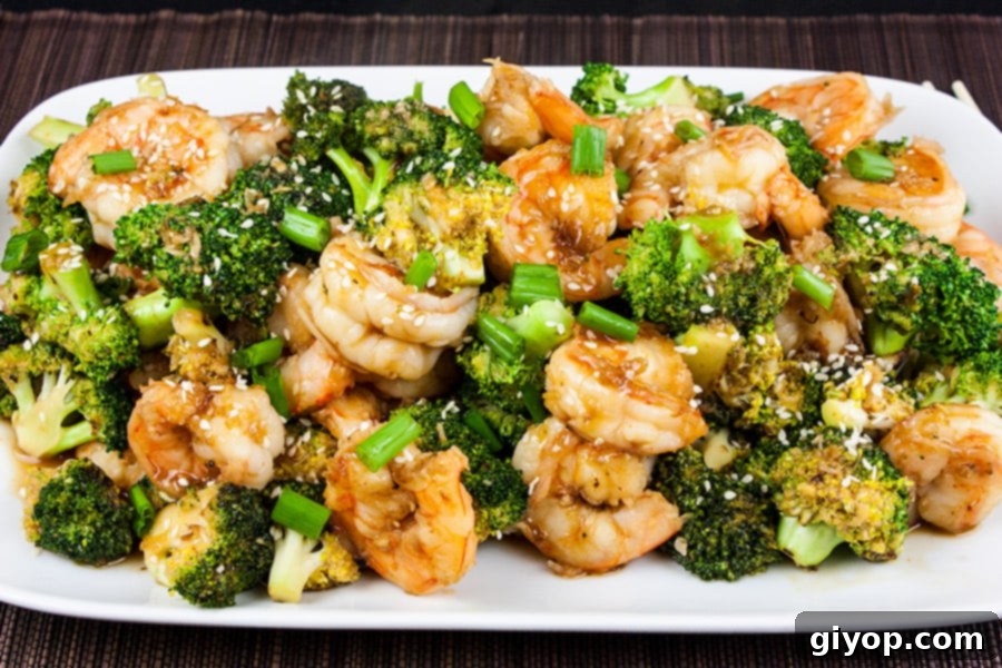 Savory Sesame Shrimp and Broccoli 4 Shrimp and Broccoli Stir Fry on a white platter garnished with sesame seeds and green onions, close-up.