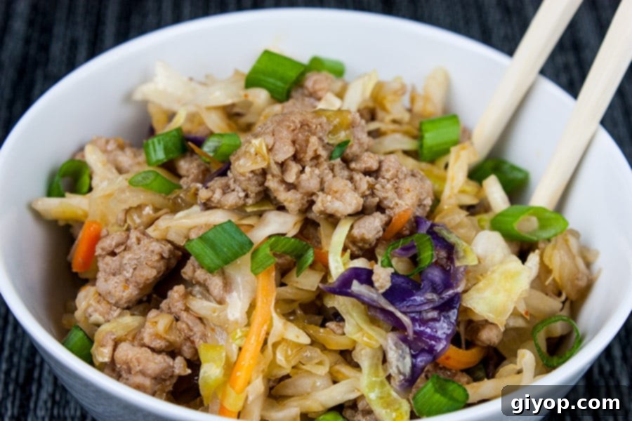A vibrant Pork Egg Roll Bowl in a white ceramic bowl, garnished with green onions and sesame seeds, with chopsticks resting on the side.