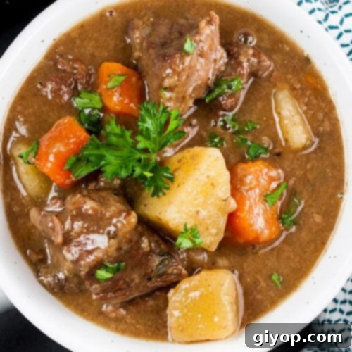 Slow cooker beef stew in a white bowl garnished with chopped parsley.