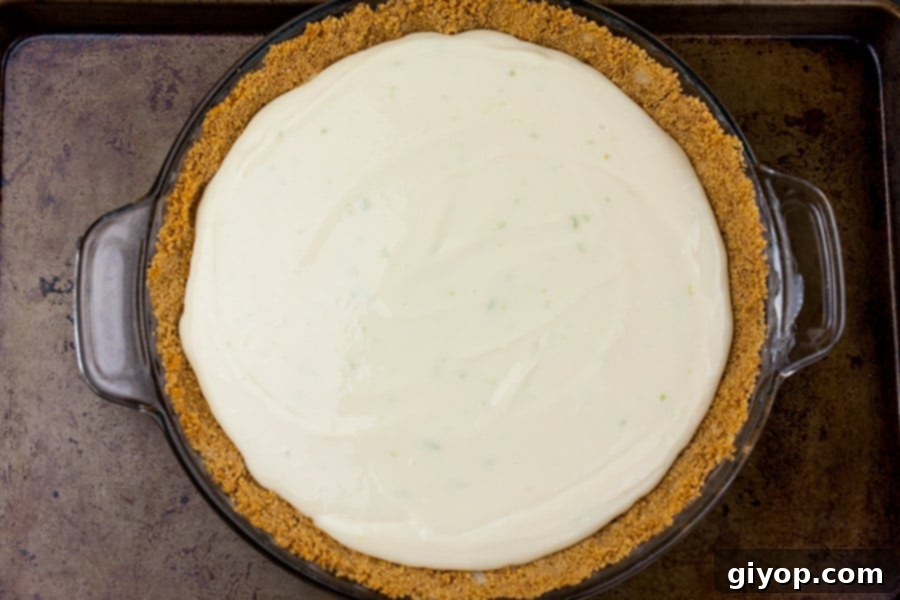 The vibrant green Key Lime Pie mixture gracefully poured into a golden-brown graham cracker crust, set within a pie pan on a baking sheet, ready to be baked to perfection.