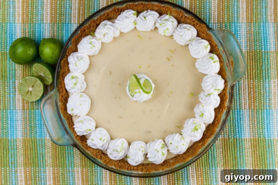 The finished Easy Key Lime Pie, generously adorned with swirls of fresh whipped cream and vibrant lime slices, presented as a centerpiece dessert. Its inviting appearance promises a taste of tropical paradise.