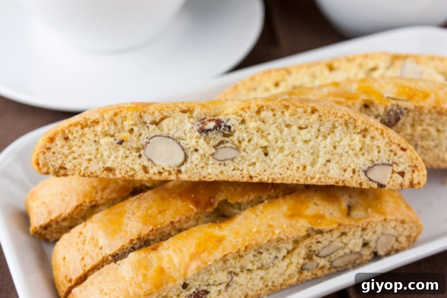 The Ultimate Vanilla Almond Biscotti 2 Almond Biscotti stacked on a white plate, showcasing their perfectly golden-brown exterior and generous almond pieces.