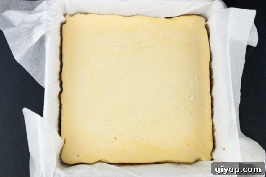 Chocolate Covered Cheesecake Bites - baked cheesecake in a parchment paper lined baking pan, ready to be chilled.