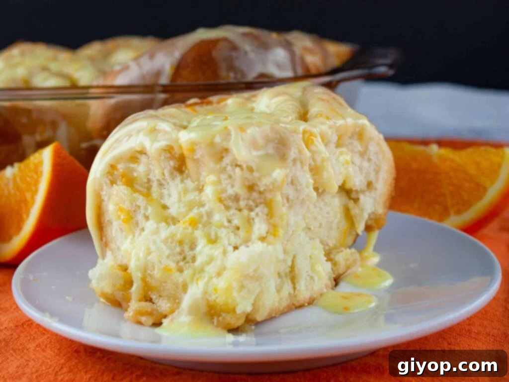 Zesty Orange Swirls, Ready in 60 Minutes 3 Two soft and fluffy orange rolls on a white plate, glistening with sweet orange glaze and bursting with citrus flavor.