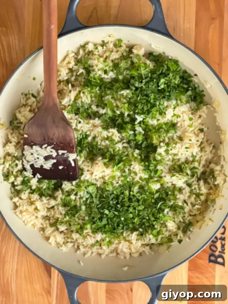 Cooked cilantro lime rice being mixed with fresh lime zest, lime juice, and chopped cilantro in a cast iron skillet.
