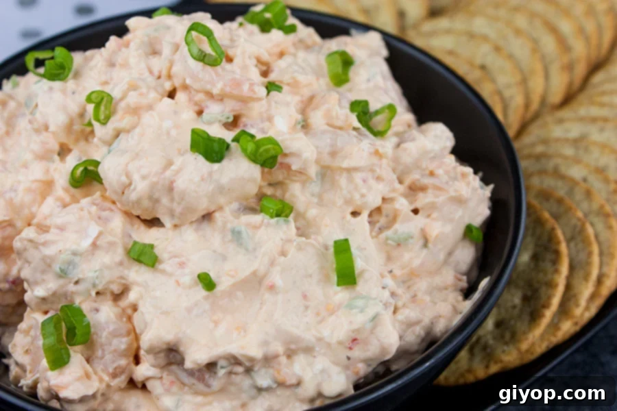 Easy cold shrimp dip in a black bowl garnished with diced green onions and surrounded by crackers.