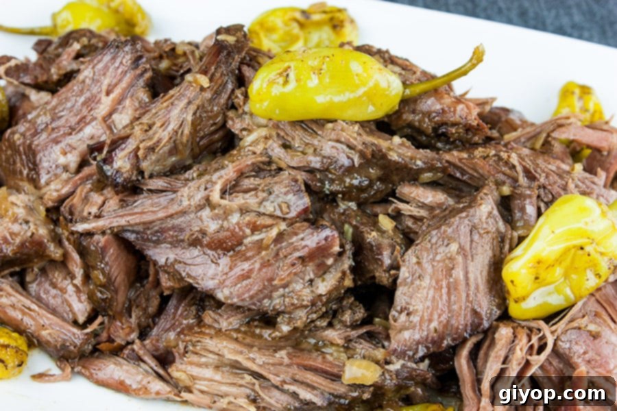 Melt-in-Your-Mouth Mississippi Pot Roast 2 Juicy Crock Pot Mississippi Pot Roast on a white platter, garnished with vibrant green pepperoncini peppers.