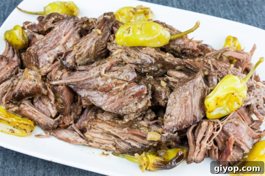 Melt-in-Your-Mouth Mississippi Pot Roast 6 A generous portion of Crock Pot Mississippi Pot Roast on a white platter, ready to be served, with pepperoncini peppers scattered around.