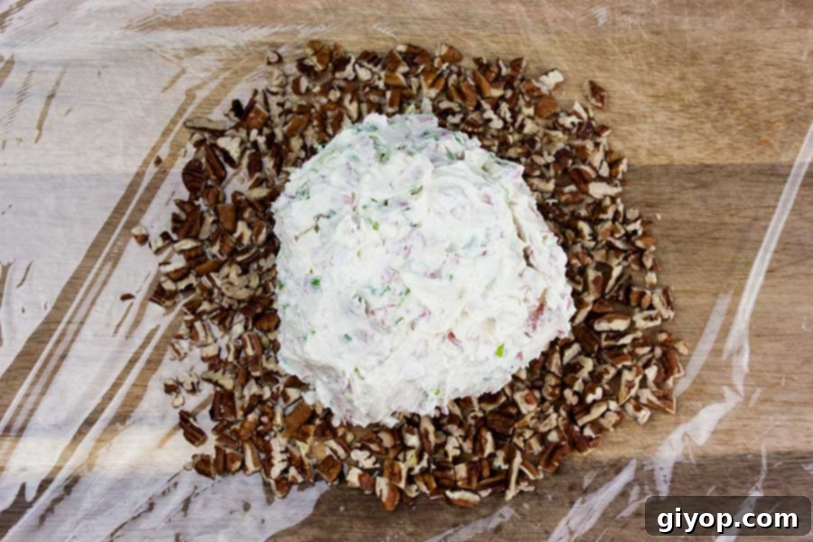 Cheese ball ingredients being mixed in a clear glass bowl with a spatula, showcasing the creamy texture and incorporated pieces.
