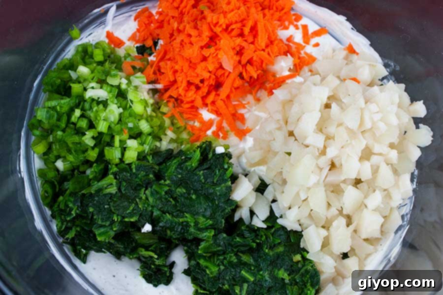 A vibrant mix of creamy base, thawed spinach, grated carrots, and finely diced water chestnuts and green onions, showcasing the fresh ingredients before mixing.