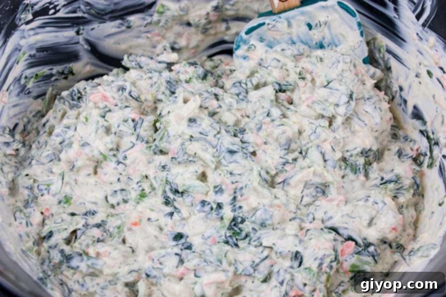 All the creamy base ingredients and dry seasonings are perfectly mixed together in a clear glass bowl, creating a smooth foundation for the dip.