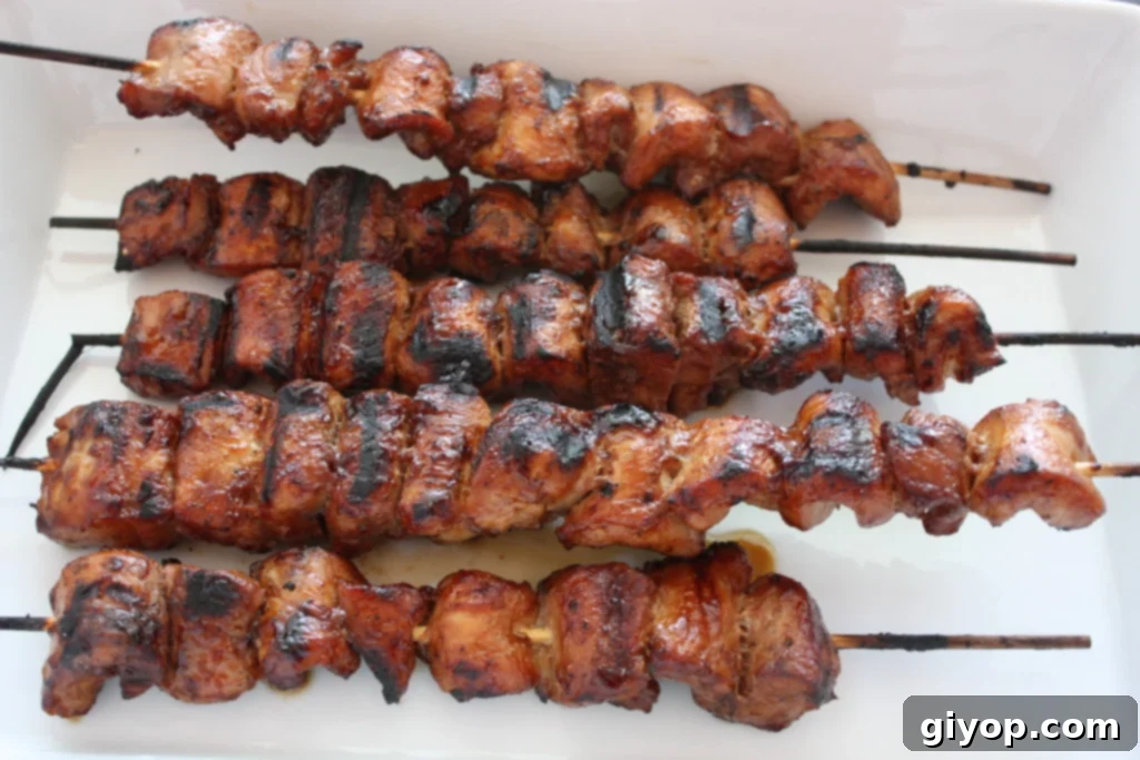 Perfectly grilled Filipino Pork Kebabs (Pinoy) skewers served on a white plate with a garnish of fresh herbs and lime wedges.