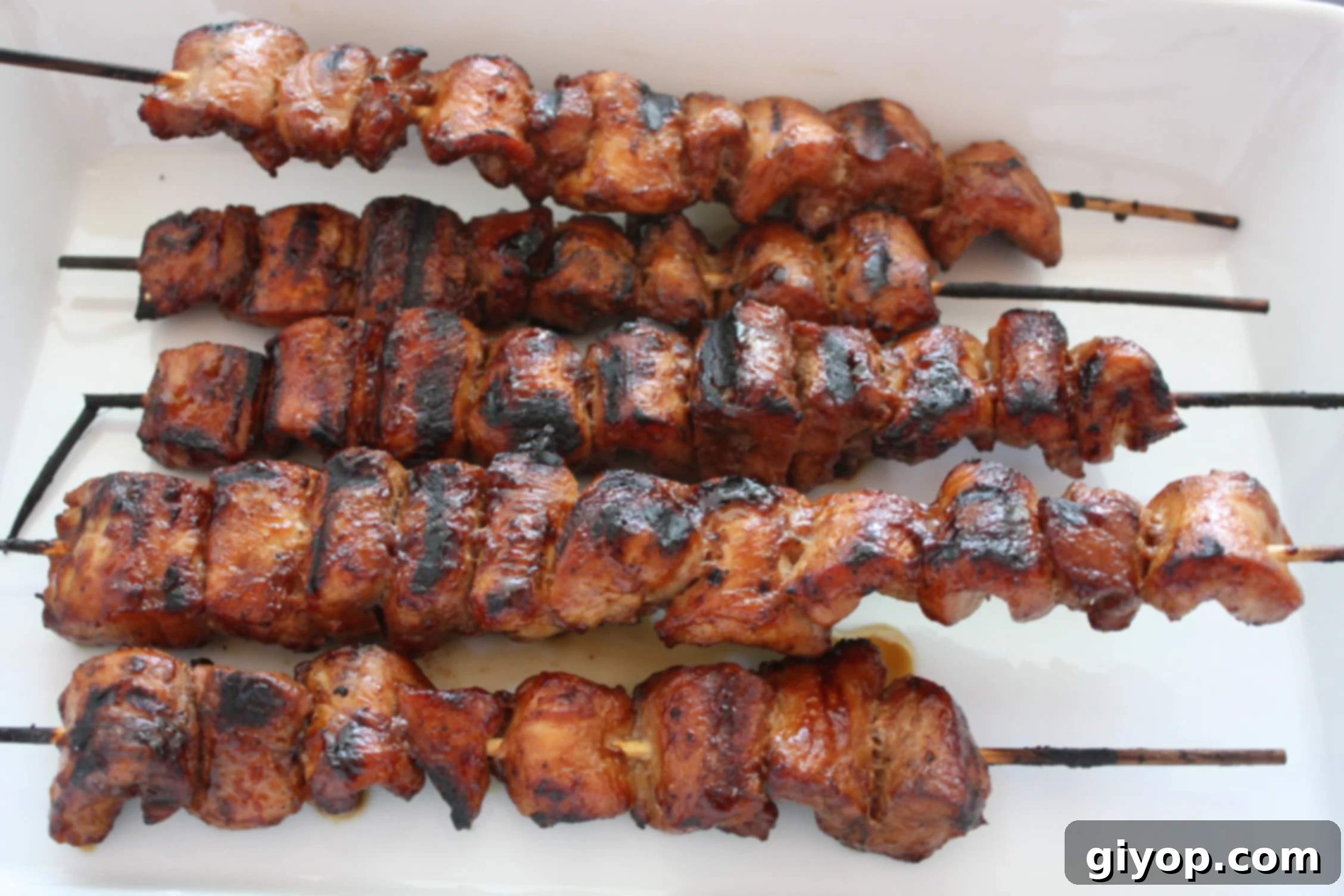 Filipino Pork Kebabs (Pinoy) skewers on a white plate, garnished with fresh herbs and a drizzle of sauce.