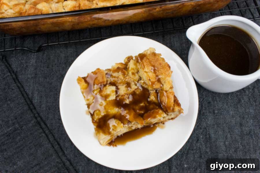Bread Pudding with Bourbon Sauce - Moist, dense yet light, kissed with classic spice flavor. This bread pudding is decadence at it's best! The bourbon sauce makes it over-the-top indulgent! Slice of bread pudding with bourbon sauce poured over the top on a white plate with extra bourbon sauce in a serving pitcher.