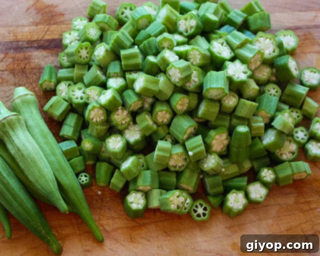 Fresh okra is neatly cut into uniform 1/2-inch pieces on a wooden cutting board, ready for the next step in preparing buttermilk fried okra.