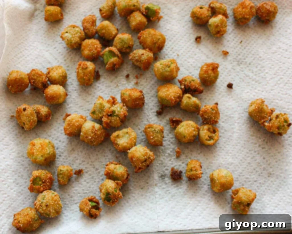 Golden-brown, crispy fried okra pieces are draining on a paper towel-lined sheet pan, indicating they are perfectly cooked and ready to serve.