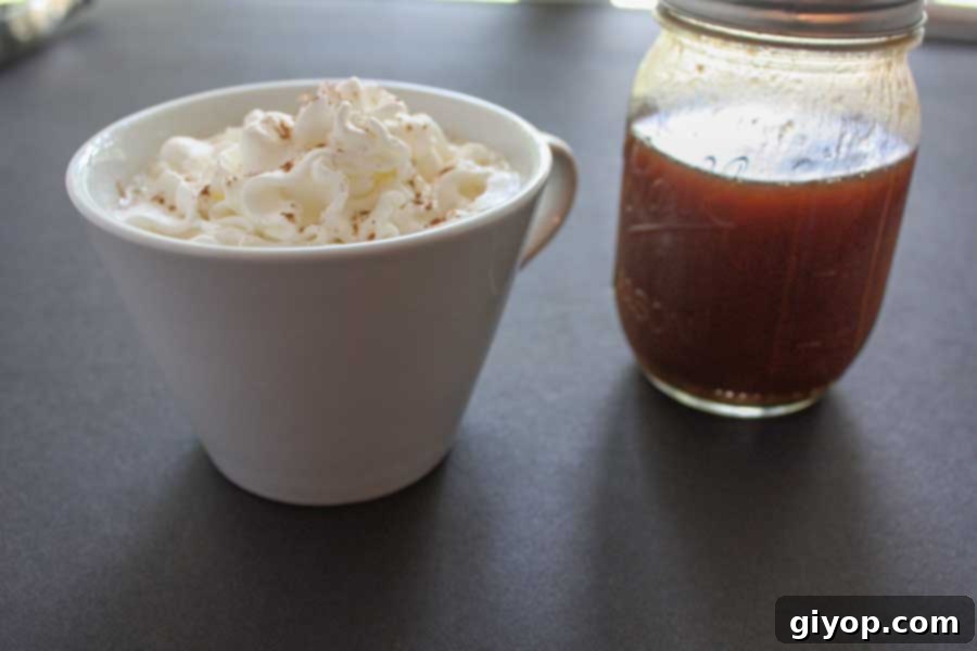 Pumpkin spice latte in a white cup topped with whipped cream and a bottle of the pumpkin syrup sitting next to it.