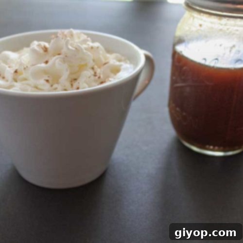 Pumpkin spice latte in a white cup topped with whipped cream and a bottle of the pumpkin syrup sitting next to it.
