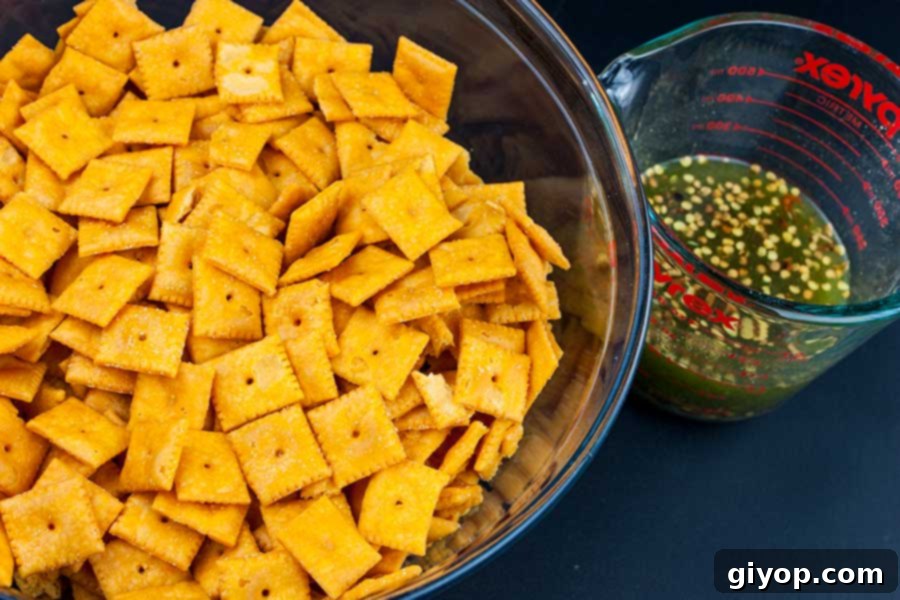 Firecracker Cheez-Itz ingredients laid out: a large glass bowl of Cheez-Itz and a smaller measuring cup containing the oil and seasoning mixture.