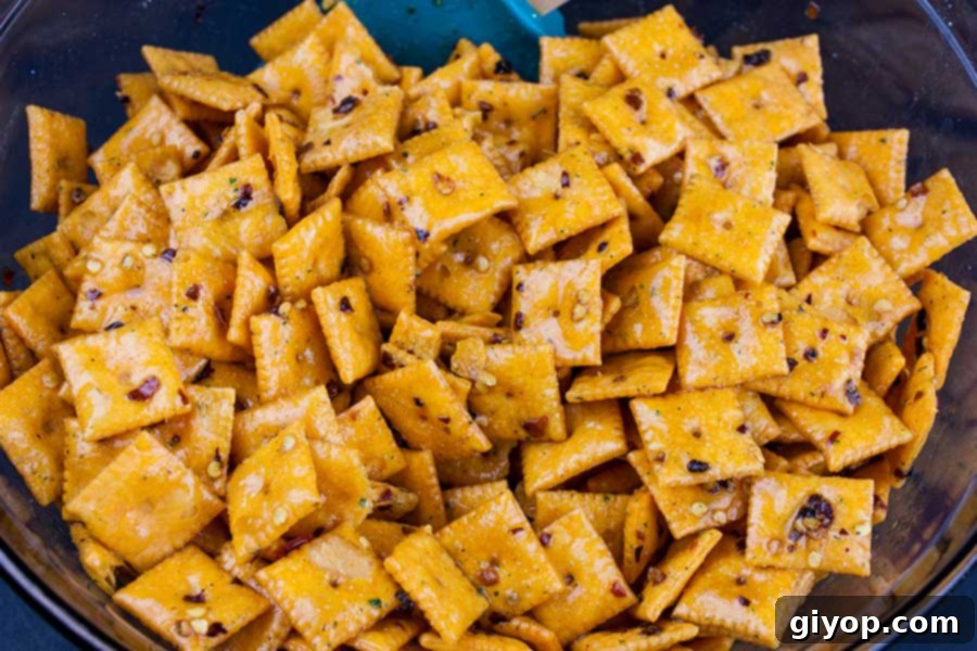 The seasoning mixture being poured over the Cheez-Itz in a large glass bowl, preparing for tossing.