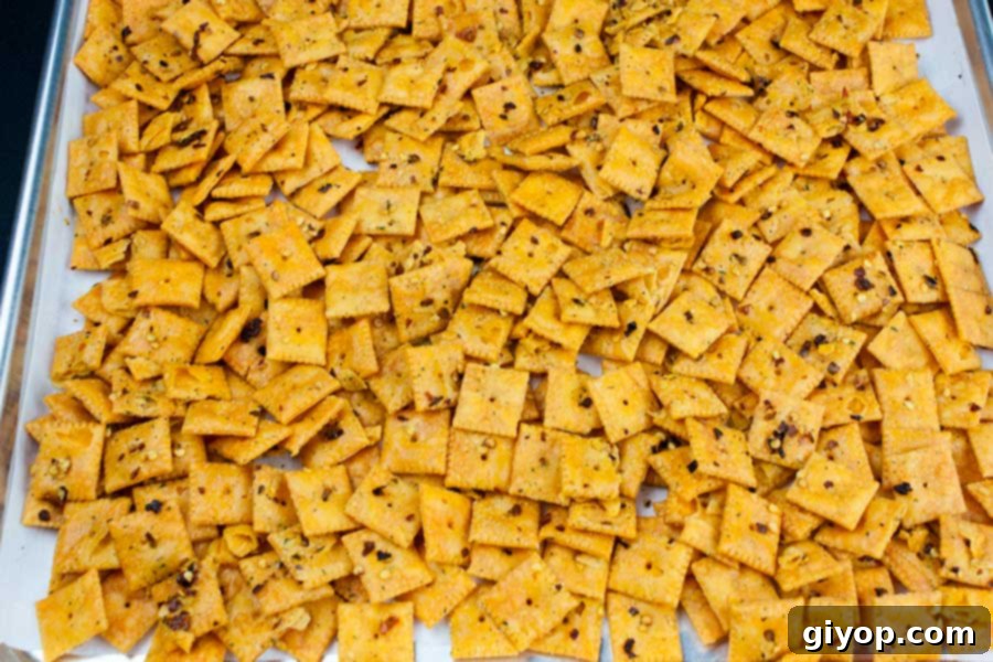 Seasoned Firecracker Cheez-Itz spread in a single layer on a parchment-lined baking sheet, ready for the oven.