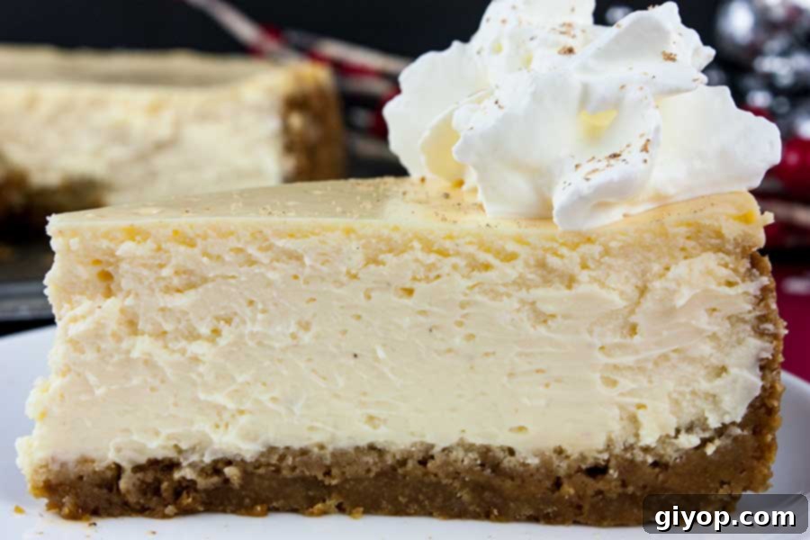 A beautifully presented slice of eggnog cheesecake with a gingersnap crust, topped with fresh whipped cream and a sprinkle of nutmeg, on a white plate.
