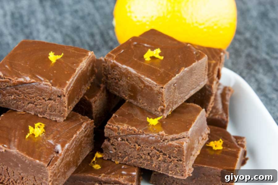 Stacked pieces of rich chocolate orange fudge, garnished with vibrant orange zest, on a pristine white plate, ready to be enjoyed.