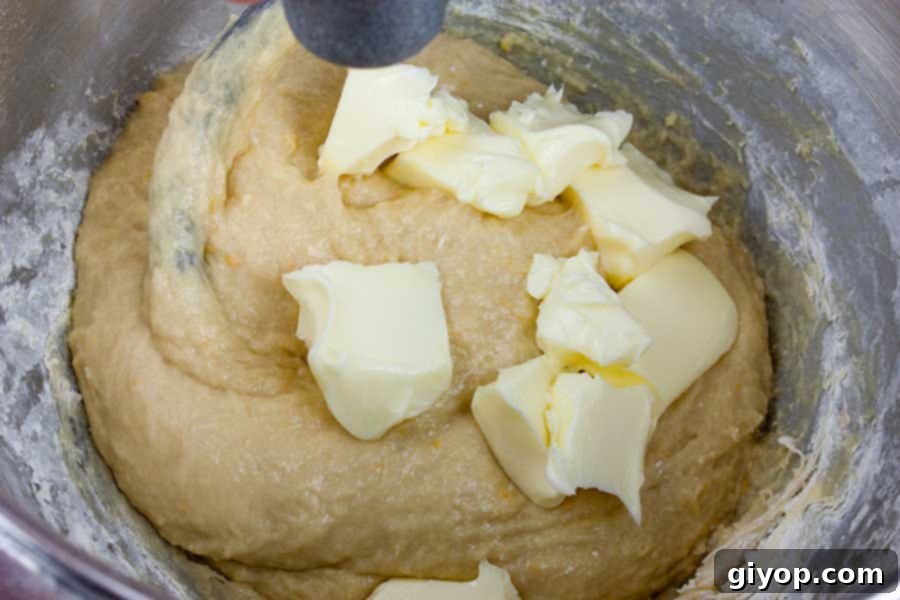 Softened butter being added to the panettone dough in a metal mixing bowl.