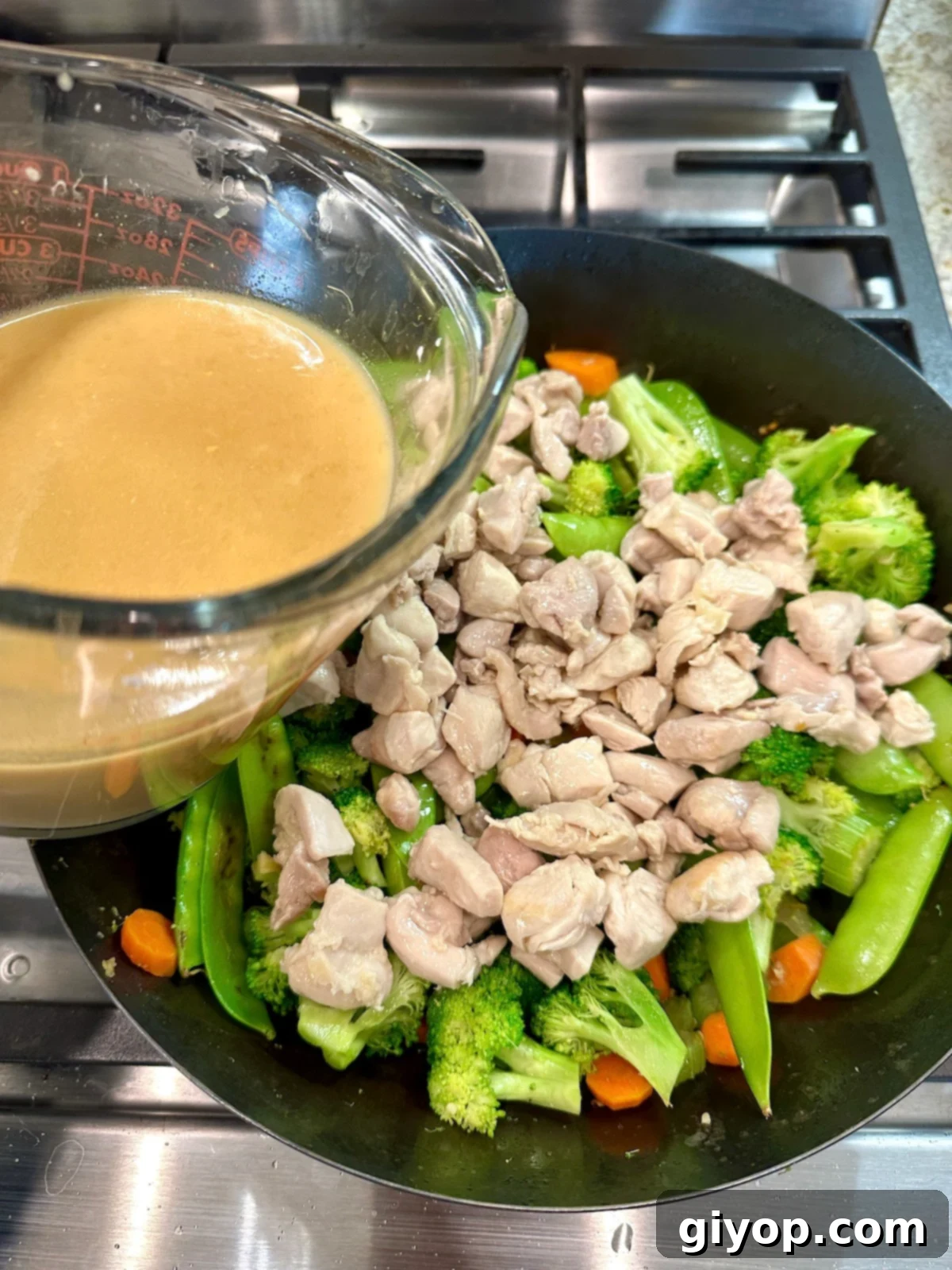 A cup of sauce for cashew chicken stir fry over a pan of veggies and chicken.