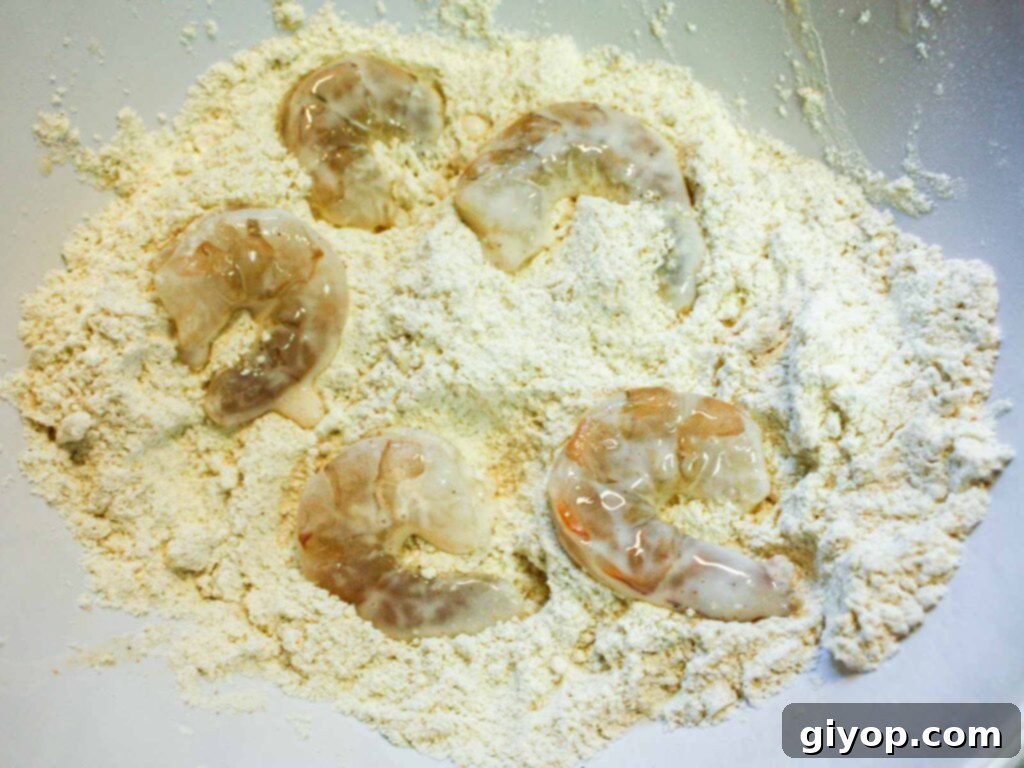 Raw shrimp fully coated in the seasoned flour and cornmeal mixture, prepared for frying.