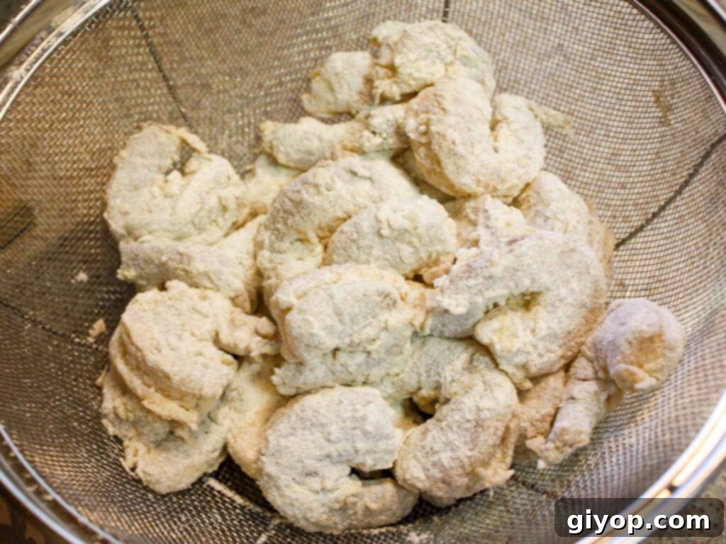 A strainer filled with battered shrimp, ready to be deep-fried to a golden crisp.