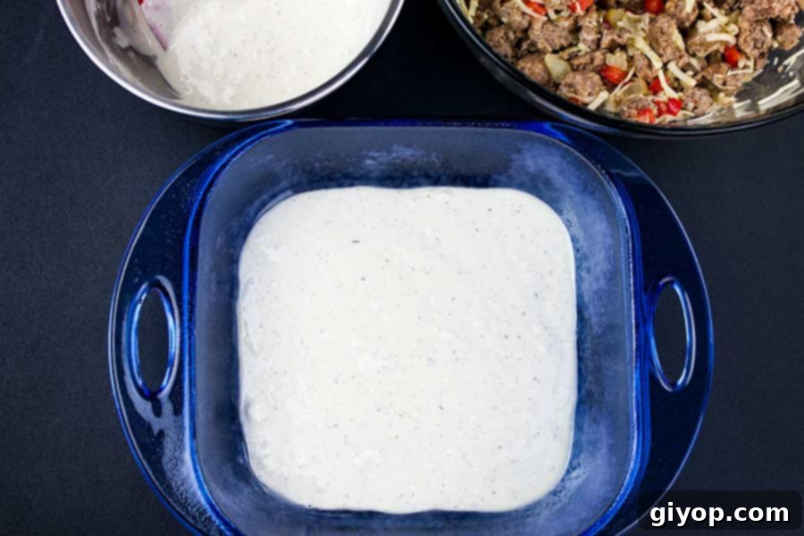 The first layer of creamy, light batter gently spread across the bottom of a blue glass baking pan, forming the base for the Sausage Breakfast Cake.