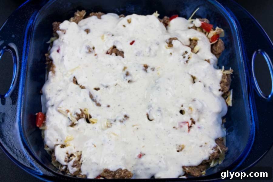 A blue glass baking pan filled with uncooked layers of light, airy batter and a savory sausage and cheese mixture, perfectly assembled and ready for the oven.