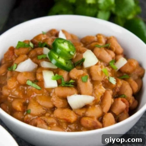 Ninja Foodi Mexican pinto beans (charro beans) in a white bowl with a jalapeno and onion garnish.
