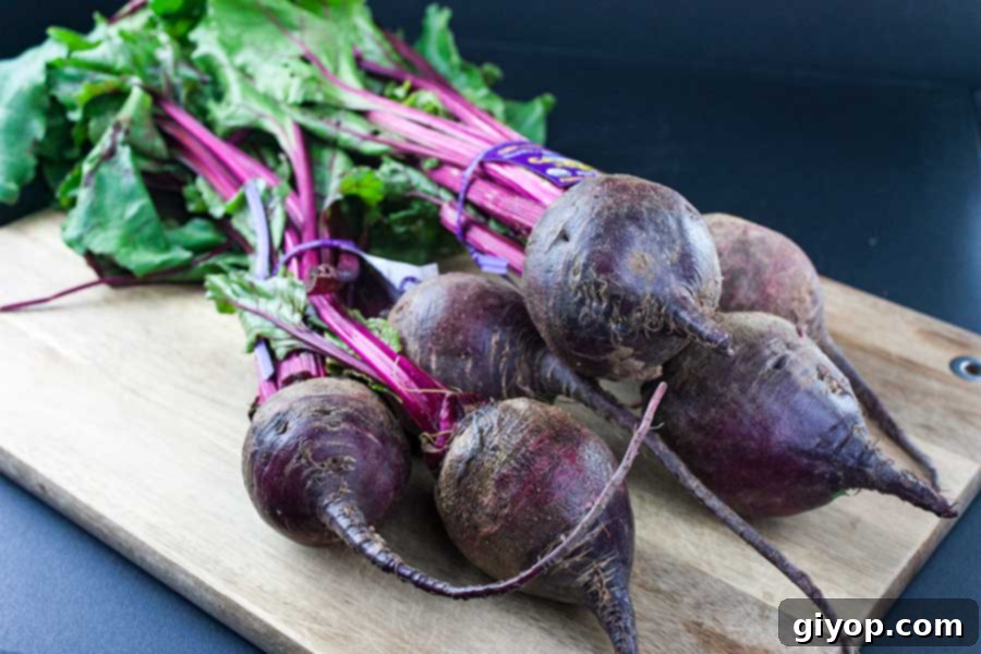 Fresh, raw beets with their lush green tops still attached, resting on a rustic wooden cutting board, showcasing their natural beauty before cooking.