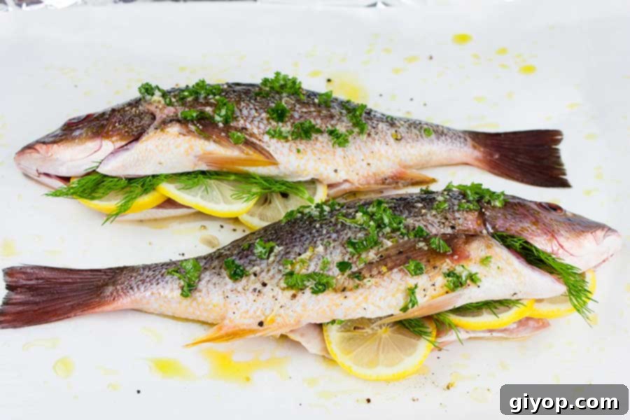 Baked Whole Red Snapper - Deliciously seasoned with citrus and herbs this red snapper recipe is on the table in minutes! Easy and healthy! Two whole red snappers, meticulously prepped with fresh herbs and seasonings, laid out on a parchment paper-lined baking sheet, ready for the oven.