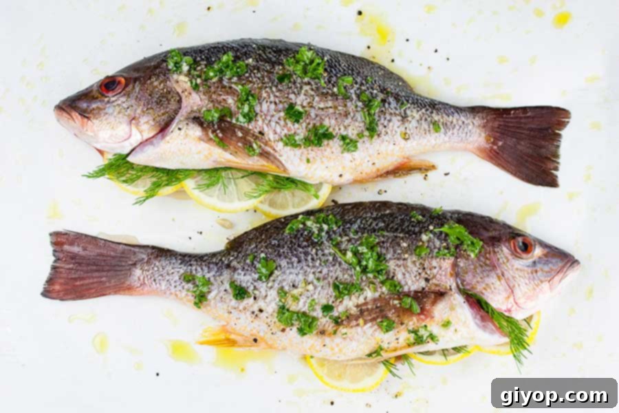 Baked Whole Red Snapper - Deliciously seasoned with citrus and herbs this red snapper recipe is on the table in minutes! Easy and healthy! Two perfectly prepped whole red snappers, adorned with herbs and seasonings, laid on a parchment-lined baking sheet, glistening and ready for the oven.