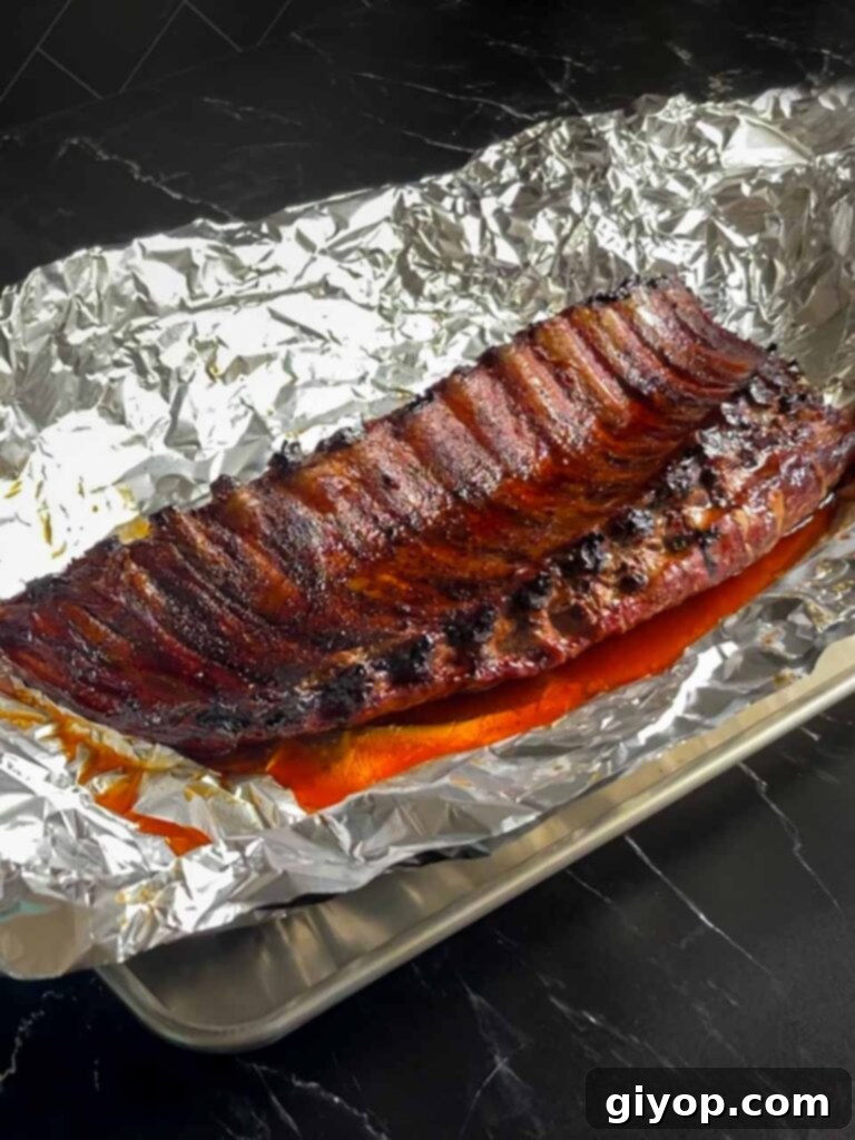 A rack of tender baby back ribs being unwrapped from aluminum foil after the braising stage, ready for the final smoke.