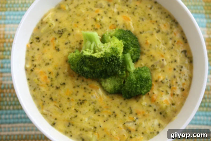 A steaming bowl of homemade creamy broccoli cheddar soup garnished with fresh broccoli florets and shredded cheddar cheese.
