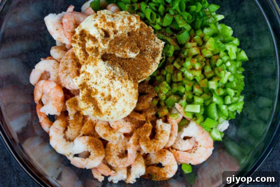 Freshly cooked shrimp, diced celery, and chopped green onions combined in a large glass mixing bowl, ready for the dressing.