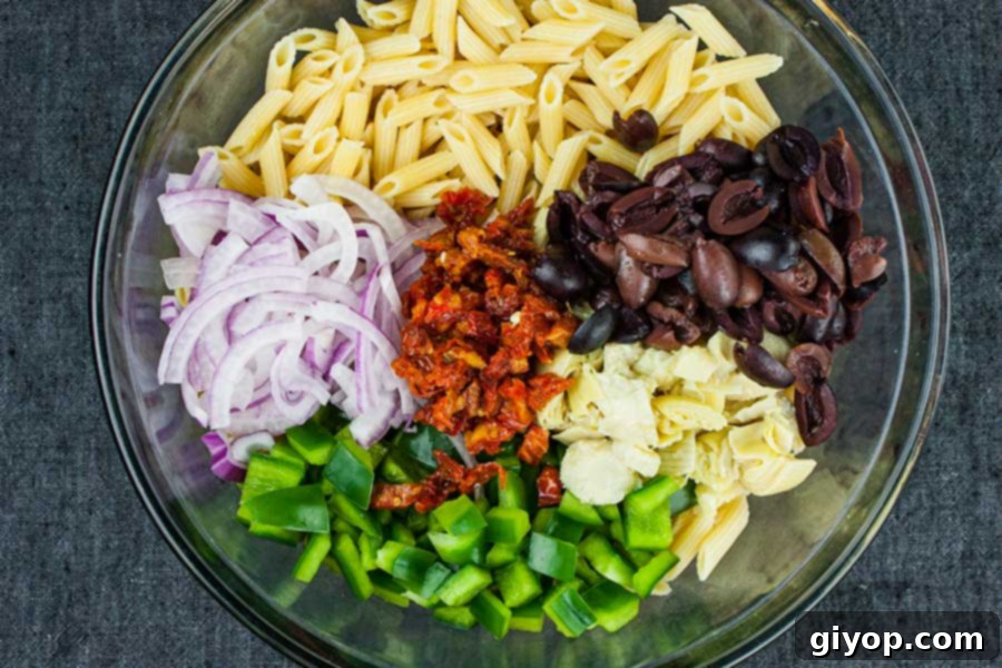 Zesty Greek Pasta Salad 3 Ingredients for Greek Pasta Salad laid out, including pasta, olives, vegetables, and feta cheese.