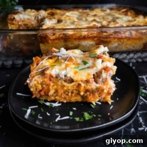 Ultimate Oven-Baked Spaghetti Delight 14 A serving of baked spaghetti garnished with fresh parsley and grated Romano cheese on a dark plate, placed on a rustic dark surface.