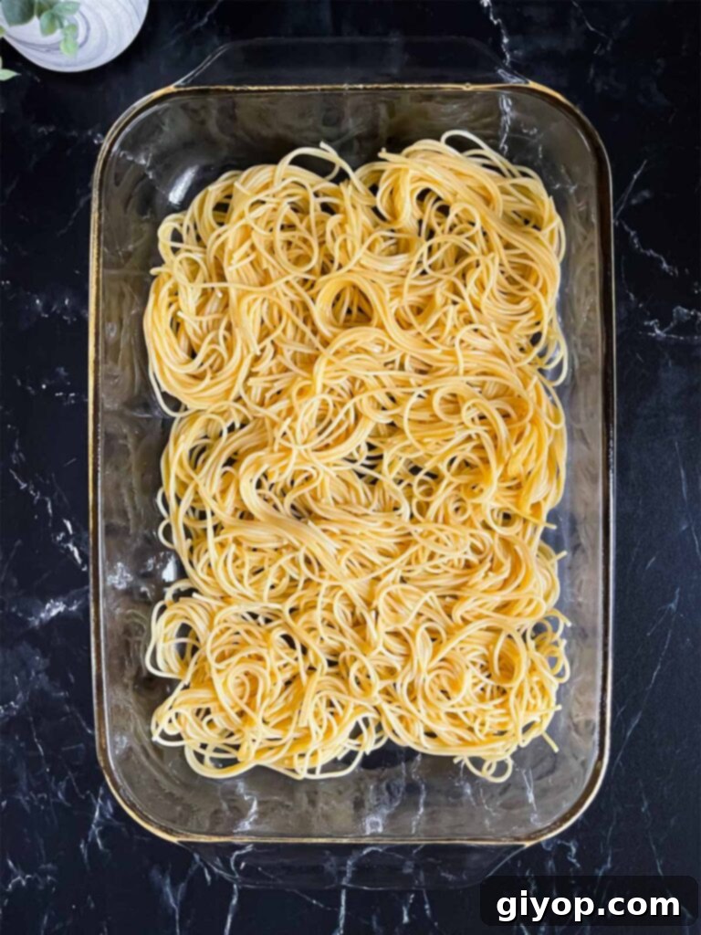 Ultimate Oven-Baked Spaghetti Delight 9 The first layer of egg-coated spaghetti noodles evenly spread in a glass baking pan.
