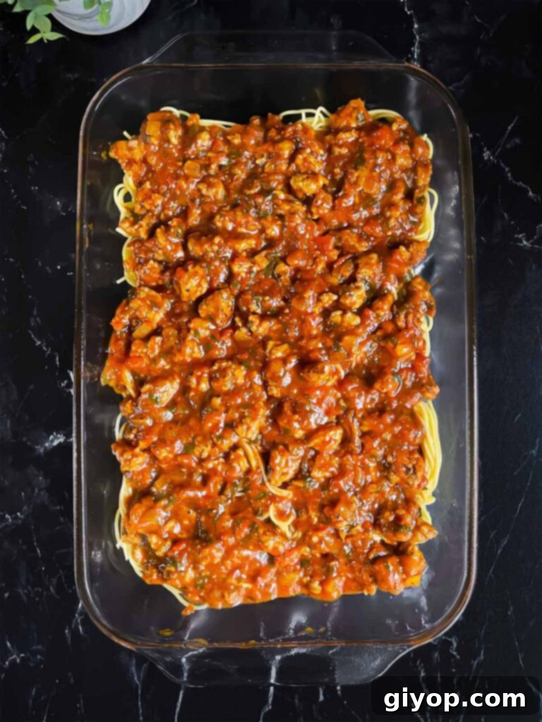 Ultimate Oven-Baked Spaghetti Delight 10 A layer of marinara sauce spread over the spaghetti in a glass baking pan, forming the next layer of the casserole.