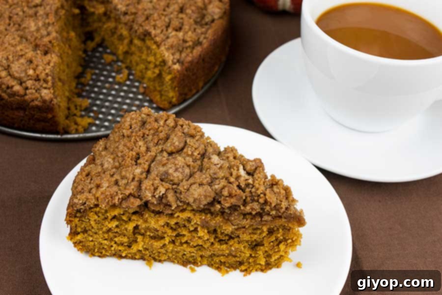 Slice of pumpkin coffee cake on a white plate with a cup of coffee in a white cup.
