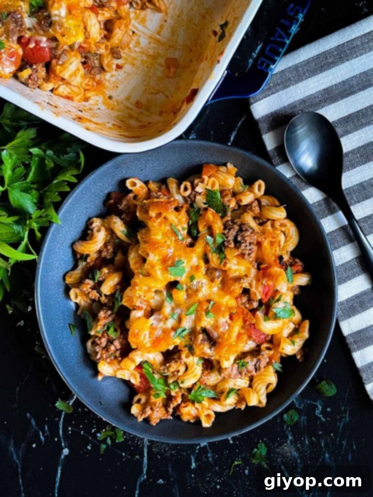 Comforting Homemade Cheesy Beefaroni 2 A dark bowl brimming with Cheesy Beefaroni, showcasing the melted cheese and pasta, with a blue casserole dish in the background.
