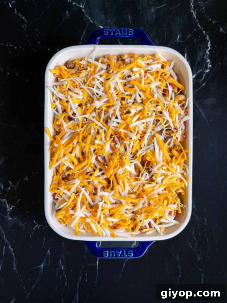 Comforting Homemade Cheesy Beefaroni 8 Cheesy beefaroni in a vibrant blue casserole dish, generously topped with a mixture of shredded cheddar and mozzarella cheese, poised for baking.